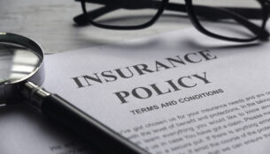Selective Focus Of Magnifying Glass,glasses And Insurance Policy Letter On A White Wooden Background.