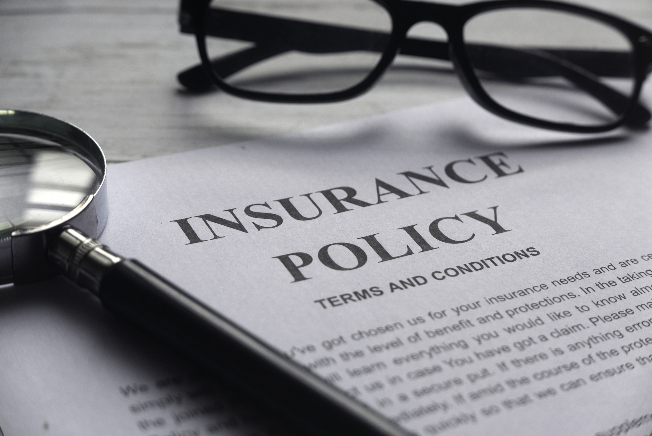 Selective Focus Of Magnifying Glass,glasses And Insurance Policy Letter On A White Wooden Background.