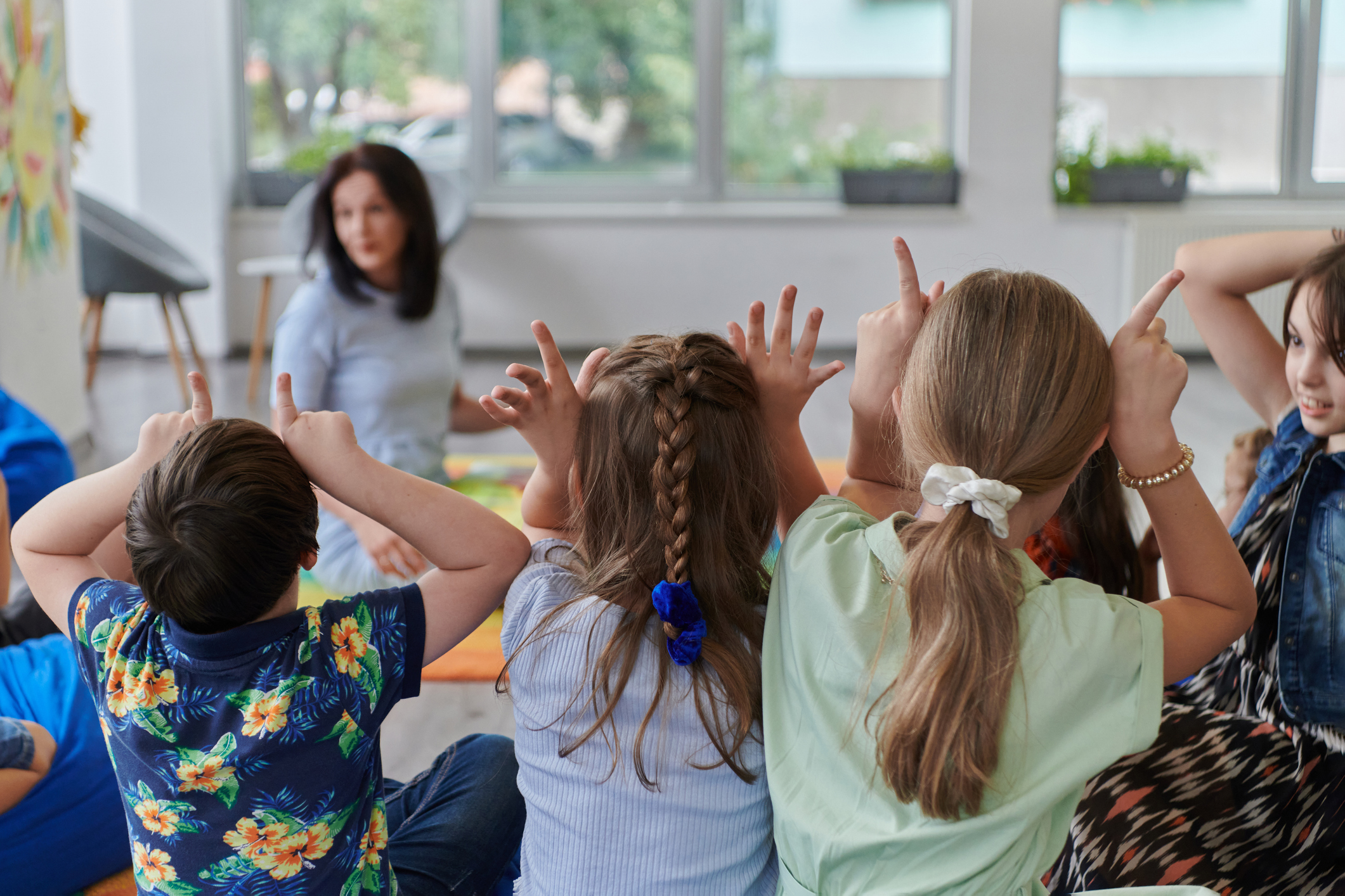 A Happy Female Teacher Sitting And Playing Hand Games With A Group Of Little Schoolchildren
